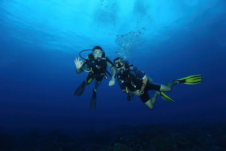 Two divers in blue water giving the OK signal