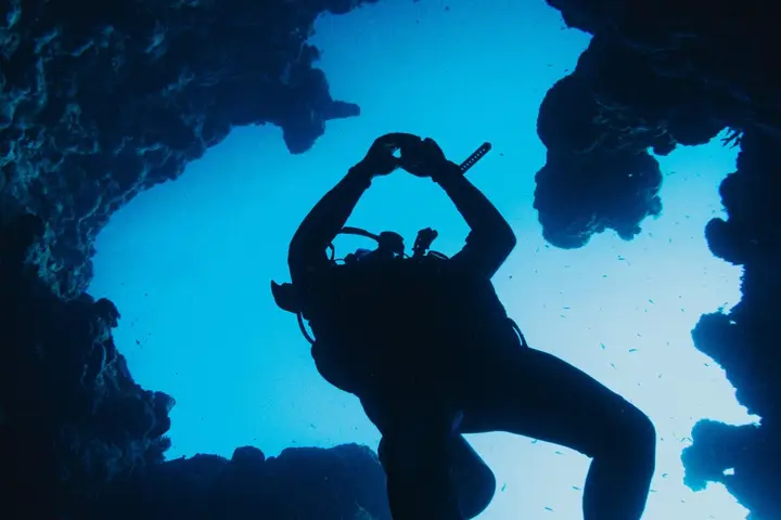 A diver silhouetted in an underwater cave against blue water